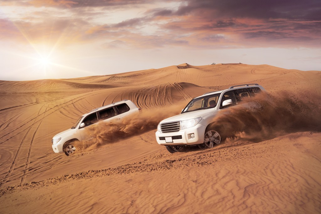 Two 4WD vehicles driving over sand dunes in the Dubai Desert