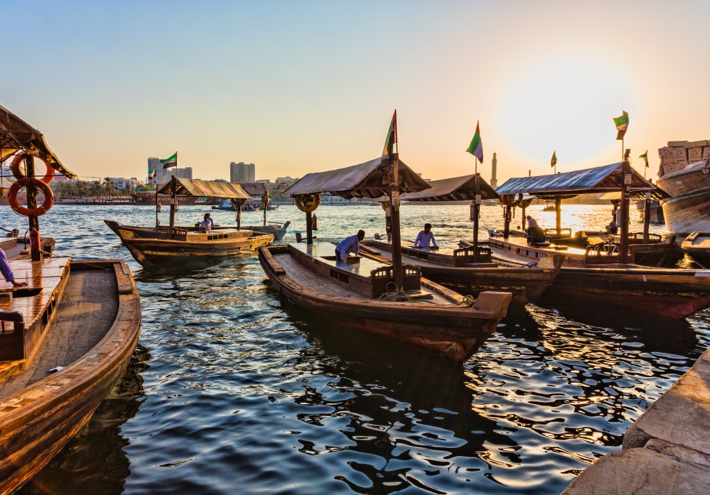 Traditional abra boats in Old Dubaifloating along the river with the sun setting in the background