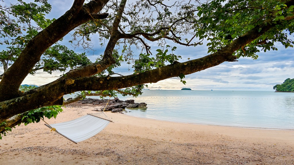 A hammock hanging from a tree next to the ocean at Island Escape by Burasari, on the island of Koh Maphrao (Coconut Island), one of the best beach resorts in Phuket, Thailand.