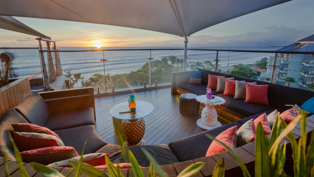 A view of the sun setting over the ocean from an alfresco couch area of Rooftop Sunset Bar at Double-Six Luxury Hote, one of the best rooftop bars in Bali - Luxury Escapes