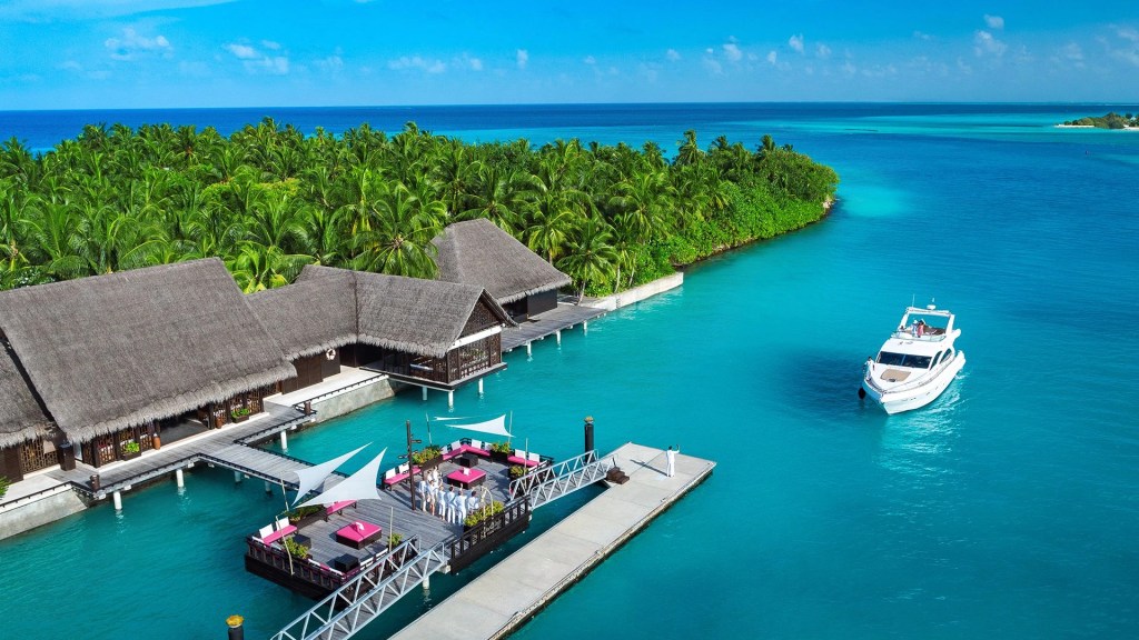 Beautiful oceanfront arrival One&Only Reethi Rah, one of the most luxurious resorts in the Maldives, with a boat leading to the island pier - Luxury Escapes