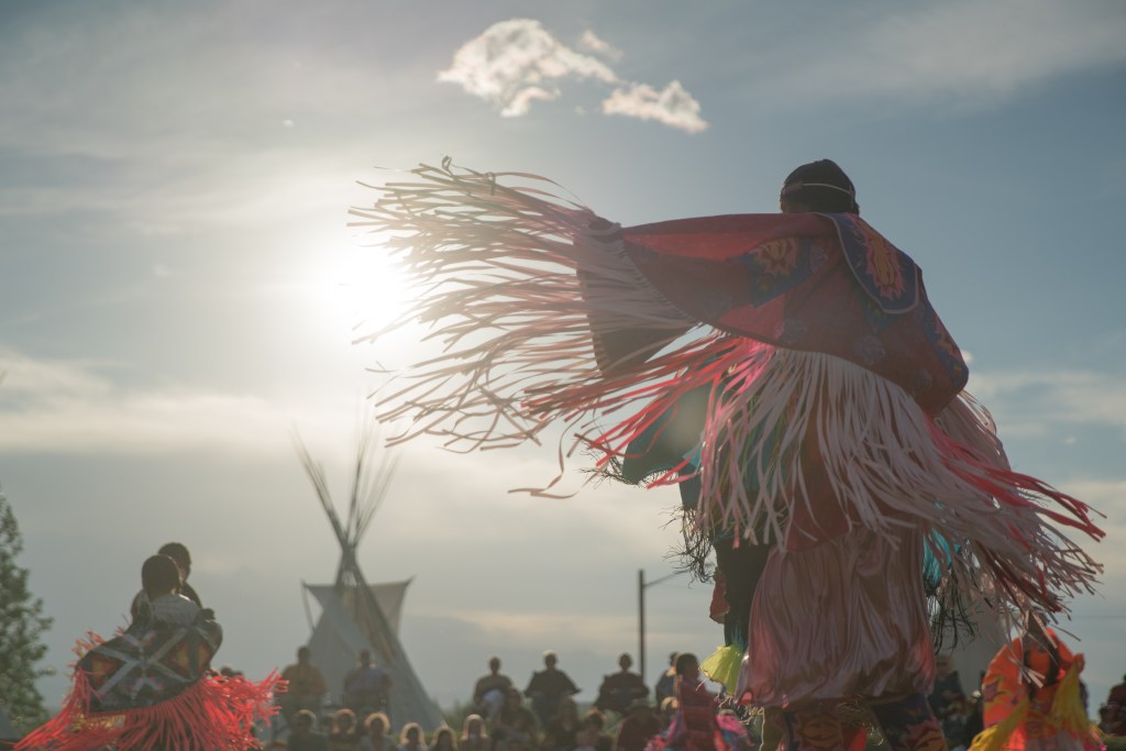 An image of Native American's dressed in traditional clothing and dancing to show their culture in the USA - Luxury Escapes