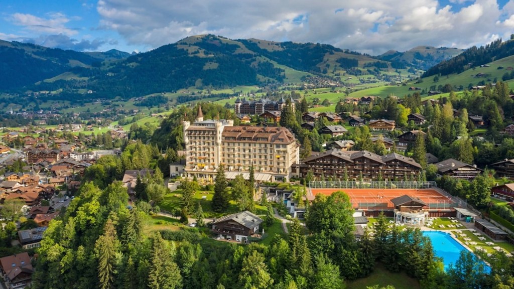 Gstaad Palace is captured surrounded by lush hills and forest and is one of the most extraordinary heritage hotels - Luxury Escapes